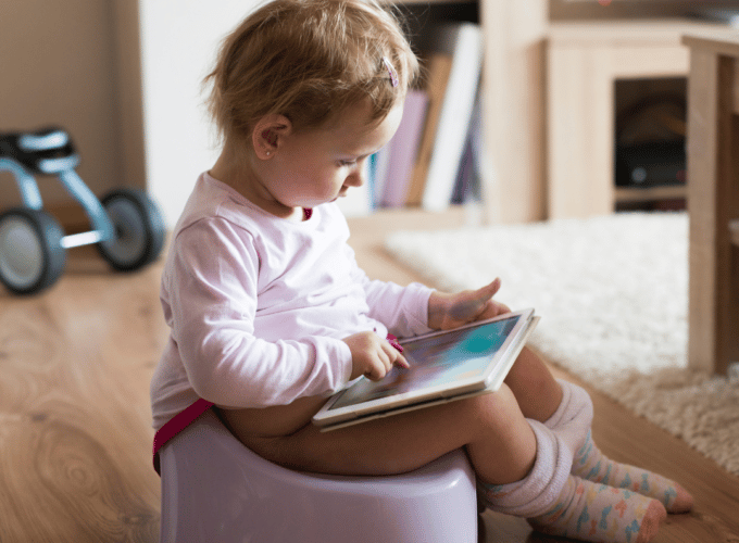 Baby reading a book whilst sitting on a potty