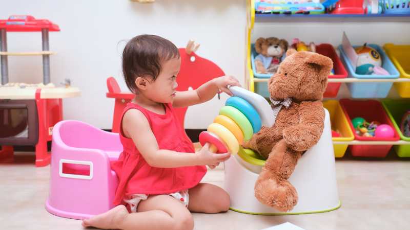 Toddler playing with a teddy bear sat on a potty